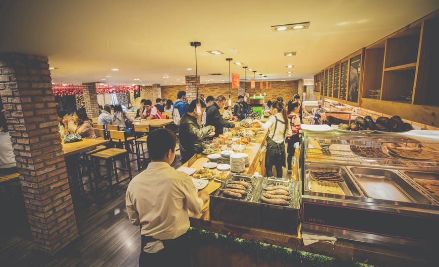 Quầy buffet L’angfarm với dãy khay món và khách đang lấy đồ ăn