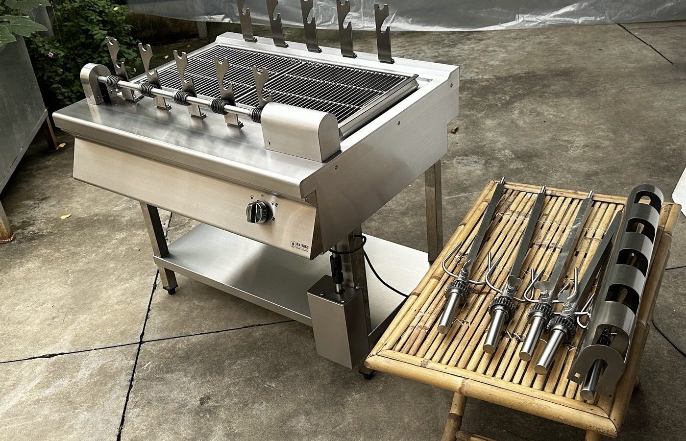 Lò nướng than trục xoay 5 xiên Hà Tiên cùng bộ xiên inox và giá đỡ bày trên bàn tre