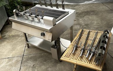 Lò nướng than trục xoay 5 xiên Hà Tiên cùng bộ xiên inox và giá đỡ bày trên bàn tre