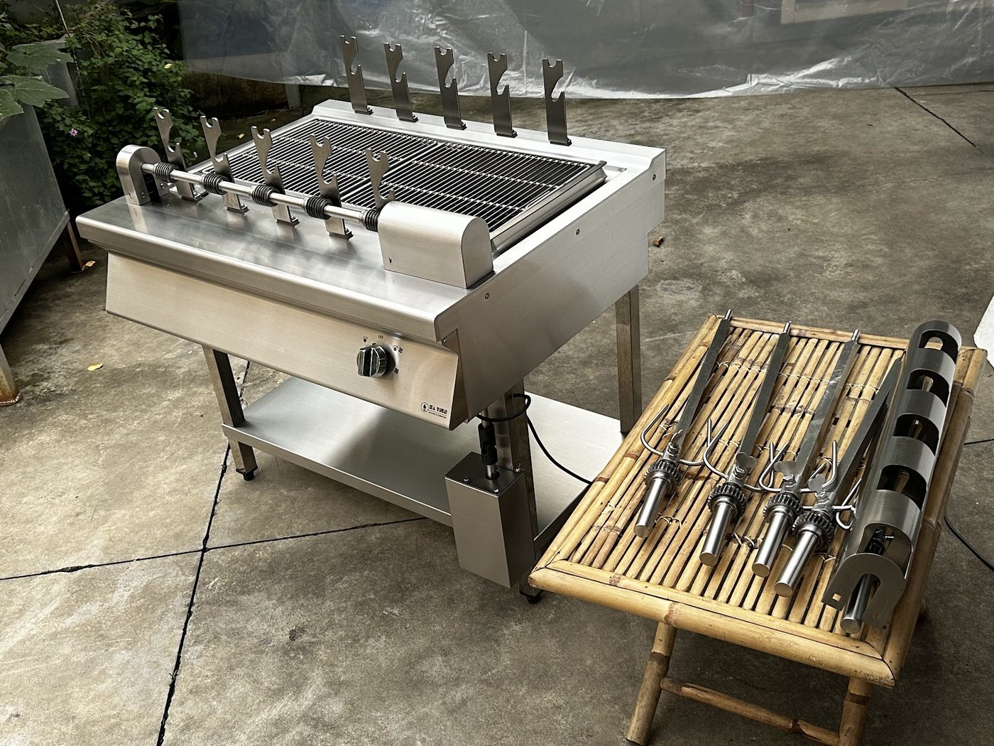 Lò nướng than trục xoay 5 xiên Hà Tiên cùng bộ xiên inox và giá đỡ bày trên bàn tre