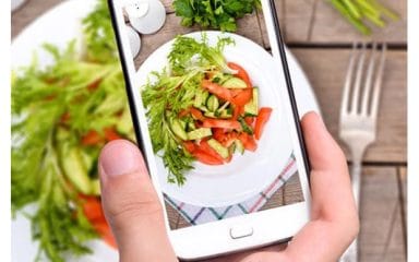 Điện thoại trên tay đang chụp đĩa salad rau củ nhiều màu bày trên bàn gỗ