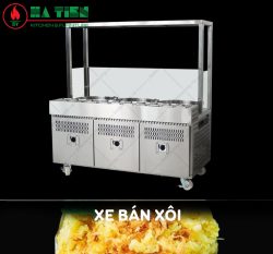 Xe bán xôi inox có mái kính, dãy khay tròn giữ nóng trên mặt, ba cánh tủ dưới và bánh xe