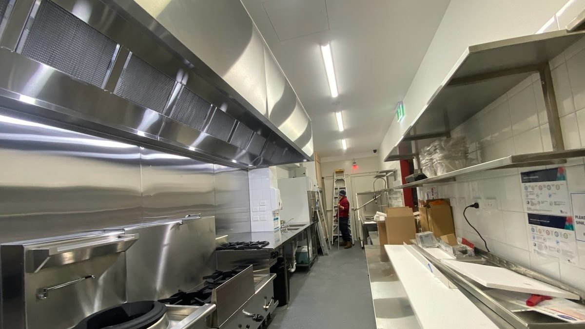 Bếp nhà hàng do Hà Tiên lắp đặt tại Melbourne: chụp hút inox chạy suốt tuyến, dãy bếp á và bếp gas, bàn cùng kệ inox hai bên