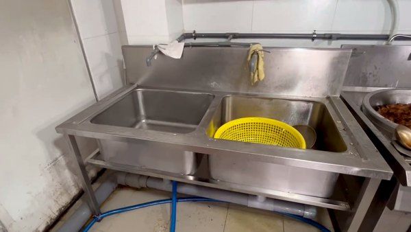 Chậu rửa inox hai ngăn đặt sát bàn để khay món đã nấu chín trong bếp ăn công nghiệp