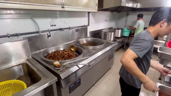 Khu bếp nấu bếp ăn công nghiệp: hai chảo lớn cố định, đầu bếp đứng canh và đảo bằng sức