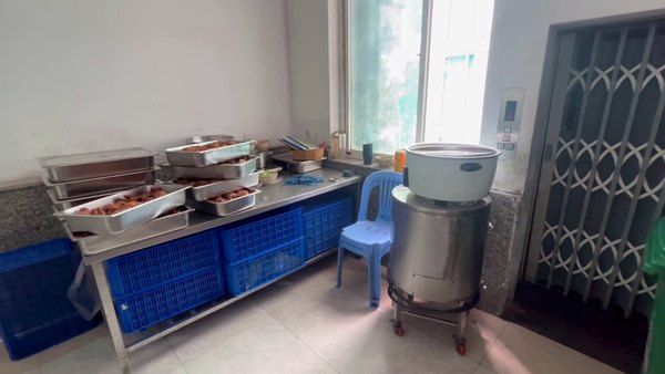 Khu chia suất bếp ăn công nghiệp: chia thức ăn trên bàn dài, khay đặt sát nhau, sọt nhựa kê dưới gầm