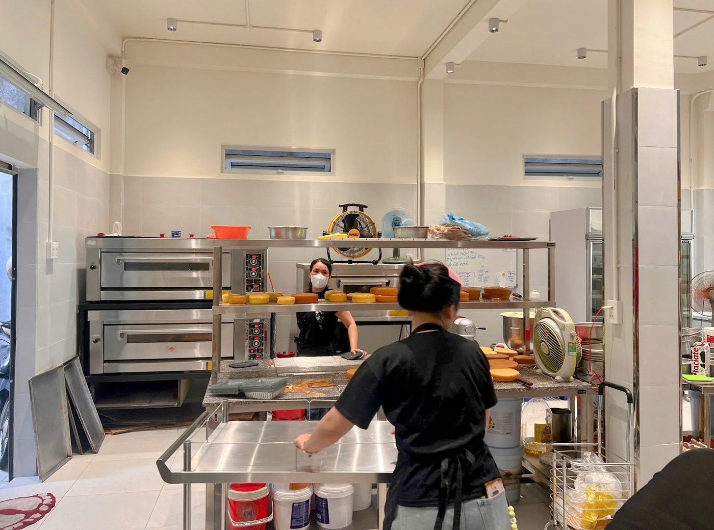 Xưởng bánh vận hành với lò nướng 2 tầng, bàn kệ inox và thợ bánh đang làm cốt bánh