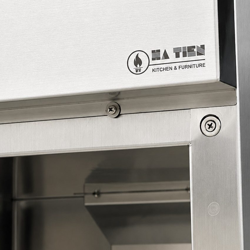 Logo Hà Tiên Kitchen & Furniture trên đầu tủ sấy chén đĩa inox, cạnh nẹp và vít bắt khung
